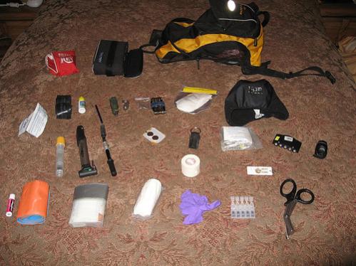 This is my version 2007.  It improved over the course of 2008, but I haven't snapped a recent pic.  I'll update as soon as I do.
Chapstick
Sam Splint
First Aid kit (bandages, dressings, pain relievers, antihistimines, sinus meds, tweezers, bandaids)
3 yard roller gauze (cling or curlex)
Nitril exam gloves
Eye drops
Trauma scissors
Small bar light
whistle
tape
visor led light
space bag
magnesium fire starter and striker
Spare batteries
Shock pump
tire pump
Epi-pen (epinepherine for anaphylactic emergencies)
Empty toothpaste tube (for repairing sidewall cuts)
Tube
Oil
Pen
multi-tool w/ plyers and knife blade
Derailleur hanger
Chain quick links and pins
Crank Brothers tool
TP
Fleece hat